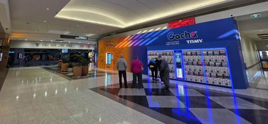 Gacha capsule store frontage inside Sunshine Marketplace, with rows of capsule machines under the illuminated Gacha sign